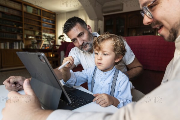 A gay couple sits with their young son in a cozy living room, focused on a tablet. They are sharing a valuable learning experience in a supportive home environment