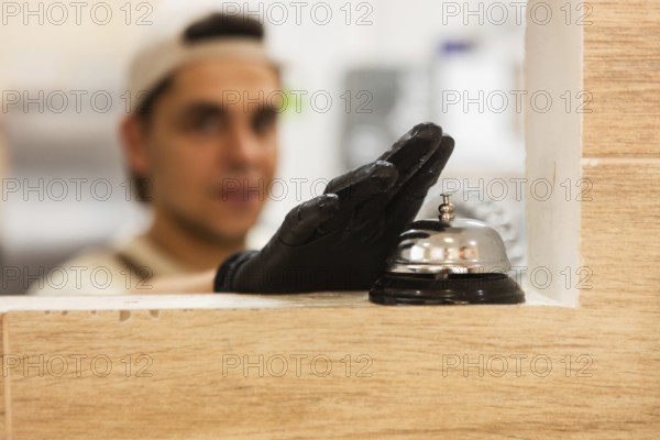 A baker wearing a glove is seen inside an Italian bakery, with a focus on a service bell on the counter The warm ambiance adds charm to the setting