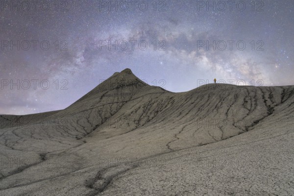 Unrecognizable lone figure stands atop a rugged hill under the starry sky of the Milky Way in the Utah desert, USA, showcasing the vastness of the universe and the solitude of nature
