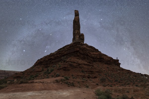 Unrecognizable silhouette of a person standing on a massive rock formation under the starry sky of the Milky Way in the Utah desert, USA. The towering geological structure under a celestial showcase highlights nature's majesty