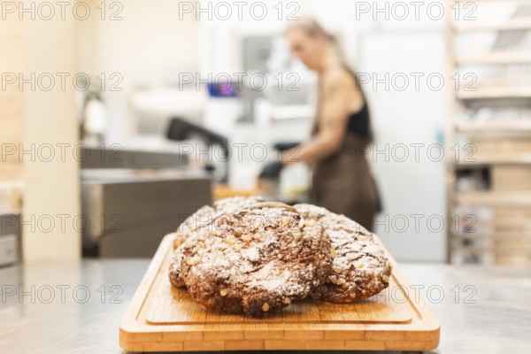 A close-up of freshly baked Italian cookies on a wooden board in a bustling bakery, with a blurred background of a person working, capturing the essence of authentic Italian baking