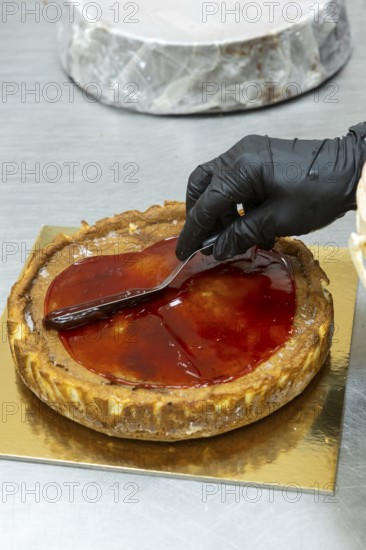 A baker wearing black gloves skillfully spreads glossy red glaze over a freshly baked tart The tart rests on a golden board, showcasing Italian pastry craftsmanship