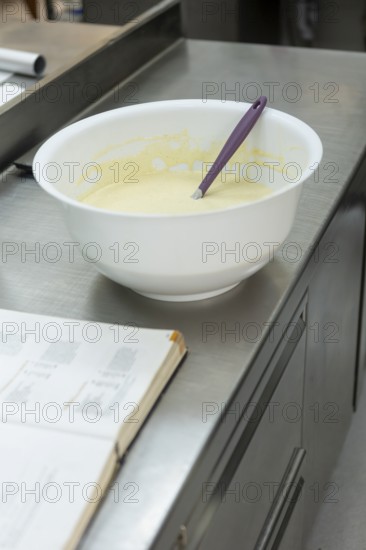 A mixing bowl with batter and a purple spatula on a stainless steel counter, next to an open recipe book Captures the essence of Italian baking preparation