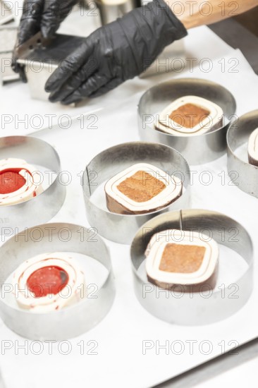 A close-up of a baker's hands wearing gloves, skillfully preparing Italian pastries in metal rings The image captures the intricate details and artistry involved in the process