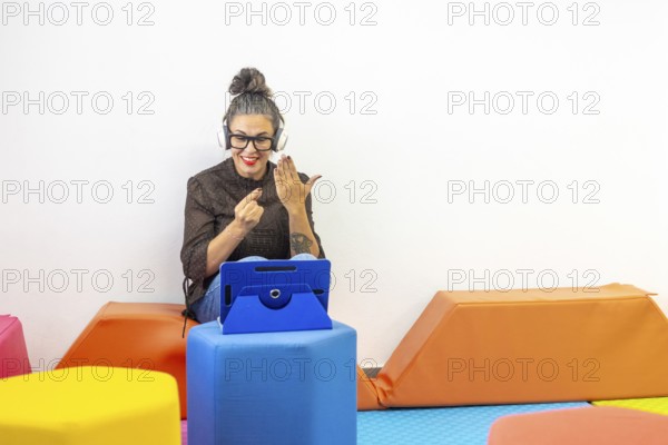 A woman with headphones and an tablet teaches sign language online, demonstrating gestures enthusiastically She sits on colorful cushions, creating an engaging learning atmosphere
