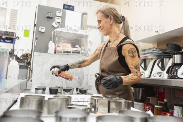A skilled baker in an apron sprays molds for pastry preparation in a professional kitchen setting The focus is on the artisan's expertise and the authentic Italian bakery atmosphere