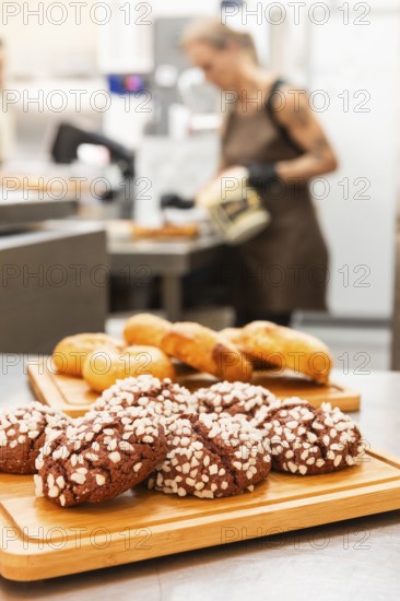 A variety of freshly baked Italian pastries are displayed on wooden trays in a bustling bakery In the background, a baker prepares more delightful treats