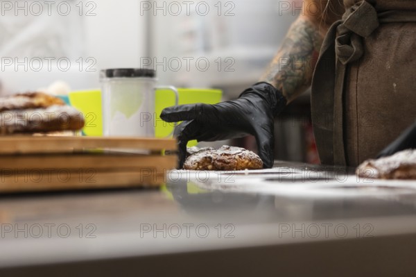 A skilled baker with tattooed arms wearing gloves arranges freshly baked pastries on a counter The warm and inviting ambiance reflects an authentic Italian bakery scene
