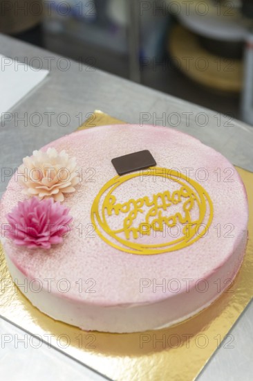 A beautifully decorated Italian cake with pink floral accents, a chocolate square, and an ornate topper Perfect for celebrations and showcasing baking artistry