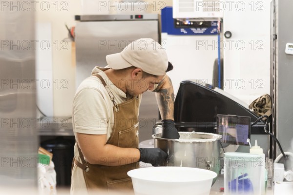 A dedicated baker in a traditional Italian bakery mixes dough in a stainless steel bowl, showcasing the art of bread making The kitchen has various bakery tools around