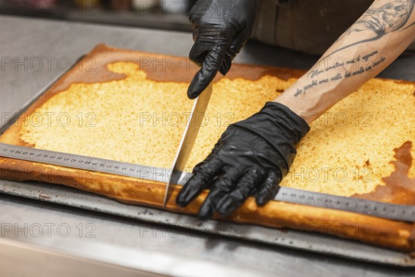 An artisan wearing gloves skillfully slices a traditional Italian cake with a large knife The large baking tray and tattooed arm create an authentic bakery atmosphere