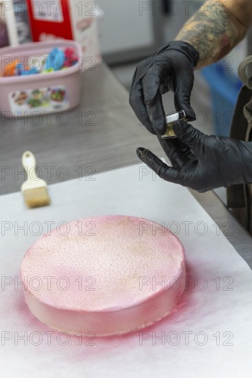 A skilled baker wearing gloves applies pink icing and gold dust to a cake in an Italian bakery The process displays the artistry and attention to detail typical of Italian baking