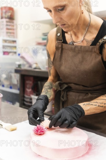 A skilled artisan wearing an apron and gloves adds delicate floral decorations to a pink pastry, showcasing the meticulous craft of Italian bakery artistry in creating elegant desserts