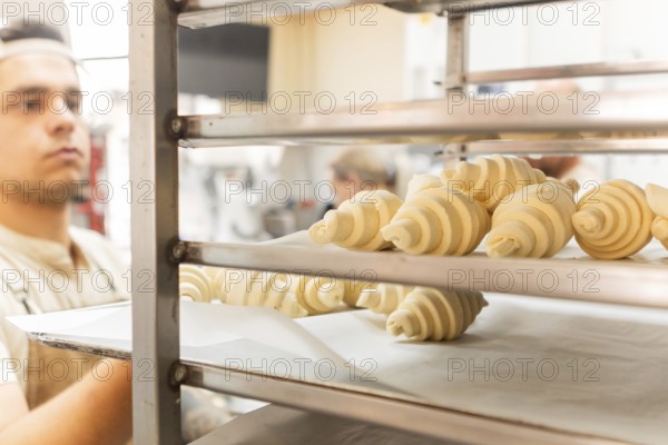 A baker carefully places freshly rolled croissants on a rack in a bustling Italian bakery The dough is perfectly formed, showcasing a blend of tradition and skill