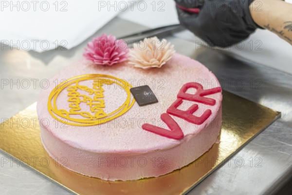 A beautifully crafted Italian birthday cake featuring pink floral decorations and a happy birthday topper, showcasing an exquisite blend of elegance and craftsmanship