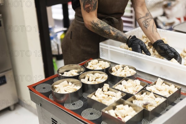 A focused baker with tattooed arms and black gloves arranges pastry pieces into metal molds, showcasing his expertise and dedication in an authentic Italian bakery setting