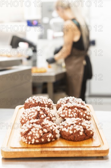 A display of freshly baked Italian pastries topped with sugar crystals on a wooden board A baker works in the blurred background, creating a cozy bakery atmosphere