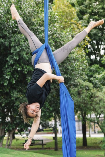Aerialist performs acrobatics on blue fabric in a lively Bogota park The scene captures the blend of artistry and athleticism against a backdrop of lush greenery