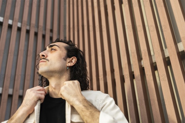 A man gazes upward with confidence, adjusting his collar against a modern architectural backdrop The image reflects a contemporary lifestyle and urban fashion sense