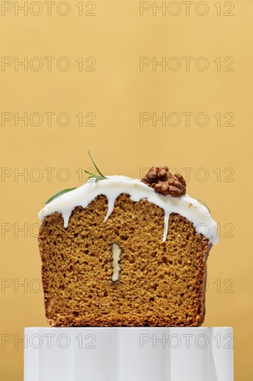 A mouthwatering carrot cake loaf with creamy white frosting sits against a warm orange background Topped with walnuts and rosemary, this dessert is a perfect treat