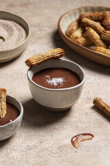 Homemade churros dipped in rich chocolate sauce, sprinkled with sugar and cinnamon, presented on a moody ceramic surface with linen background