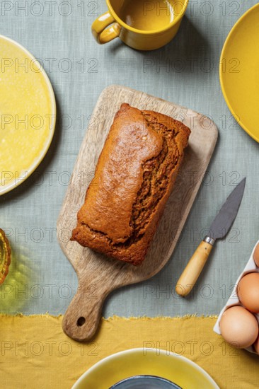 A freshly baked carrot cake loaf sits on a wooden board surrounded by a warm, autumn-themed table setting The vibrant colors and textures create a cozy and inviting atmosphere