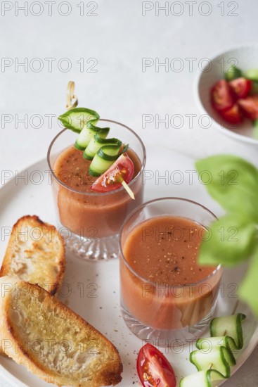 Two glasses of gazpacho garnished with cucumber and tomato skewers, served with toasted bread A fresh and colorful presentation perfect for a light meal