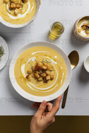 A creamy cauliflower curry soup garnished with croutons, rosemary, and drizzles of cream, served in ceramic bowls on white tile Artisan-style presentation emphasizes a homemade touch