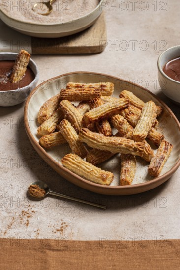 Ceramic plate of sugary churros paired with rich chocolate sauce, sprinkled with cinnamon, on a linen background