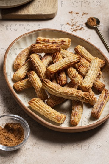 Homemade churros dusted with sugar and cinnamon, served on a ceramic plate alongside chocolate and cinnamon powder, displayed on a concrete background