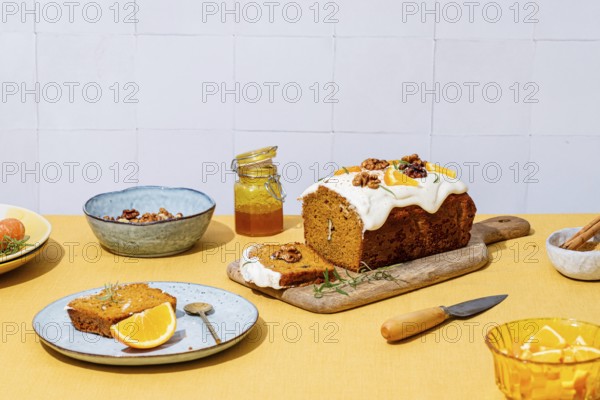 A mouthwatering carrot cake loaf topped with creamy cheese frosting, walnuts, and rosemary Vibrant yellow hues adorn the table with a rustic linen backdrop