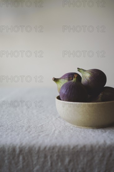A close-up of fresh figs in a rustic bowl on a textured white tablecloth, creating a serene and inviting scene Perfect for food and kitchen-themed projects