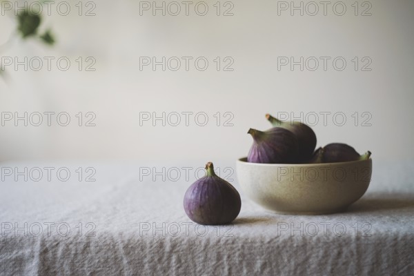 A collection of ripe figs in a ceramic bowl on a rustic tablecloth One fig is placed outside the bowl Soft, natural lighting creates a warm, inviting atmosphere