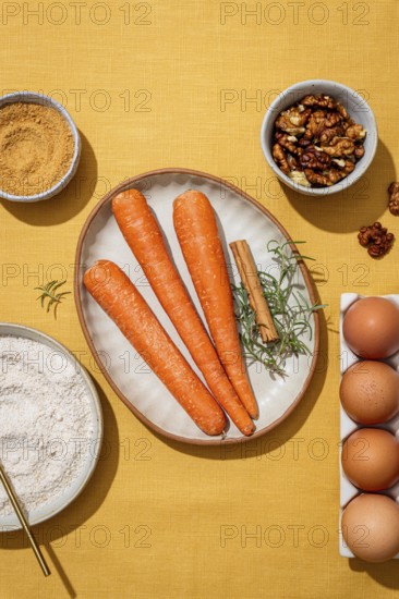 A vibrant assembly of fresh carrots, eggs, walnuts, and rosemary on a yellow linen backdrop, showcasing essential ingredients for a flavorful carrot cake loaf