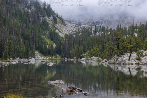 Misty atmosphere blankets a peaceful lake surrounded by dense forests and rugged mountains in the heart of Colorado's Rocky Mountains