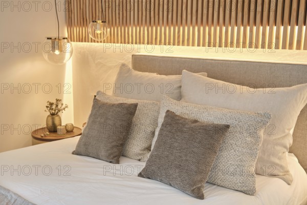Modern bedroom featuring textured pillows, soft bedding, and ambient lighting with a wooden headboard and bedside decor, embodying a serene and inviting atmosphere