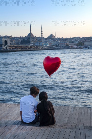 Istanbul, Turkey. 20th October 2019 A romantic couple sit beside the Golden Horn with a red heart shaped balloon at dusk, Istanbul, Turkey
