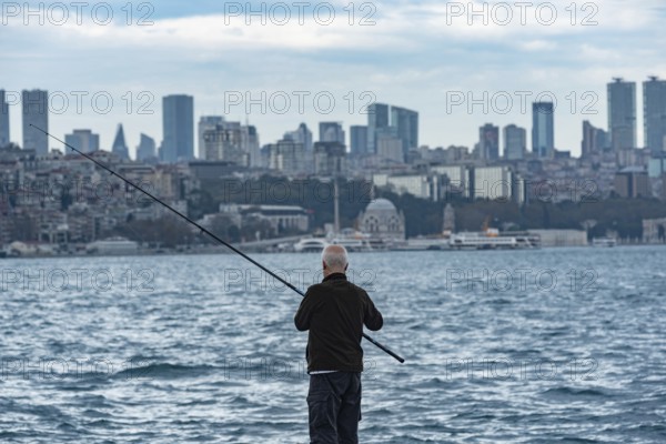 Istanbul, Turkey. November 22nd 2023 An old Turkish man fishing the Bosporus with a view of the modern European side of Istanbul in the distance, Turkey