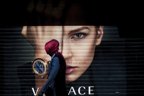 Istanbul, Turkey. April 28th 2016 A Turkish Muslim woman wearing a red Hijab walking past an advertising poster on Istiklal Street, Istanbul, Turkey