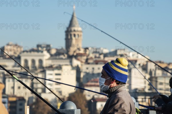 Istanbul, Turkey. November 28th 2020 A man wearing a facemask fishing from the Galata Bridge in Istanbul, Turkey during the Corona Pandemic