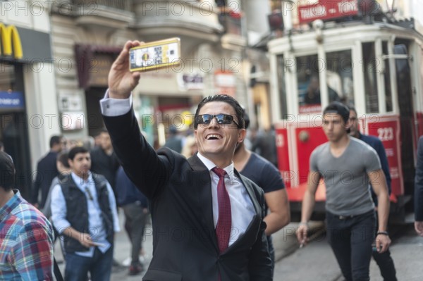 Istiklal Street, Istanbul, Turkey. March 27th 2016 A man in a business suit poses for a selfie in front of the historic tram near Taksim, Istanbul, Turkey