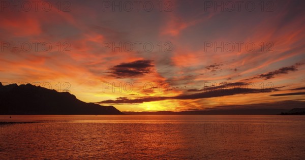 A breathtaking sunset over Lake Geneva, illuminated with vibrant shades of orange and red, with the silhouette of the Swiss Alps in the background