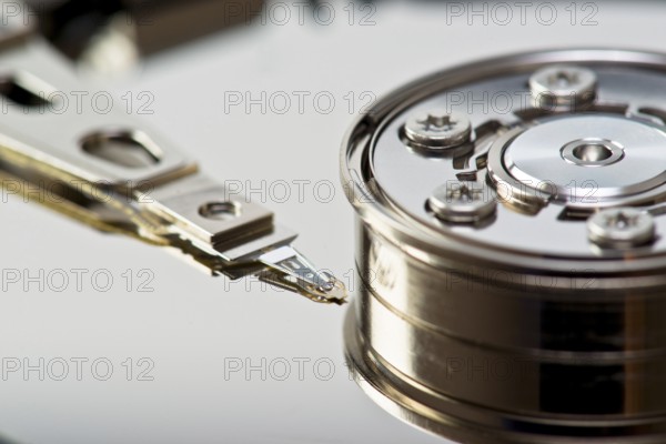 A detailed close-up image showing the read-write arm of a hard drive in precise detail, positioned above the shiny platter surface