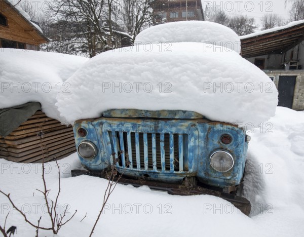 An old, rusty truck partially hidden beneath layers of thick snow in a rural winter setting in Georgia The blue paint contrasts with the white, creating a striking visual