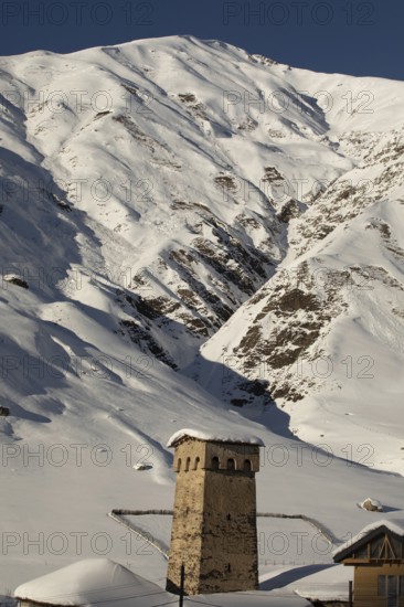 A stone tower stands amid a stunning snowy mountain landscape in Georgia The scene highlights the stark contrast between architectural heritage and natural beauty under a clear sky