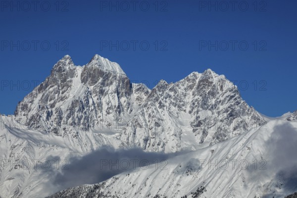 Majestic snow-covered mountain peaks tower under a clear blue sky, creating a breathtaking natural scene in Georgia Shadows and clouds add contrast to the pristine white snow