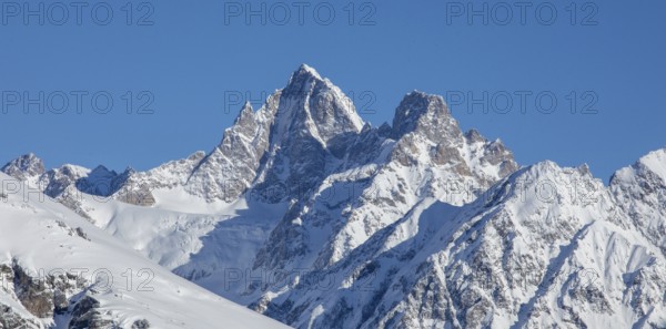 Majestic snow-covered mountain peaks rise against a clear blue sky, capturing the breathtaking beauty of nature's grandeur in a serene and pristine alpine landscape in Georgia