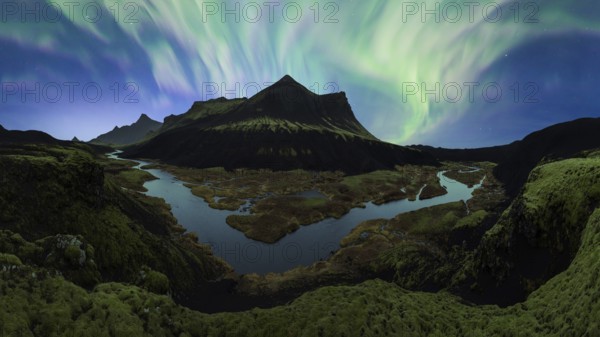 The Northern Lights unfurl in a vibrant dance across the night sky over Iceland's rugged terrain, with a serene river winding through the scene