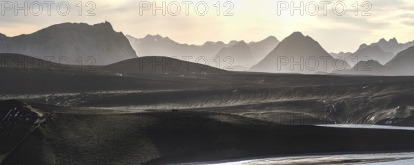 Captivating panoramic view of the Icelandic Highlands at sunset Mist gently blankets the mountains, creating a serene and ethereal atmosphere under a soft, glowing sky