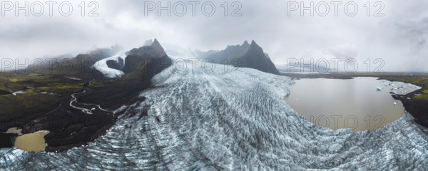 A breathtaking panoramic view of Vatnajokull National Park, showcasing the majestic glacier against a backdrop of rugged mountains and serene water bodies, under a cloudy sky